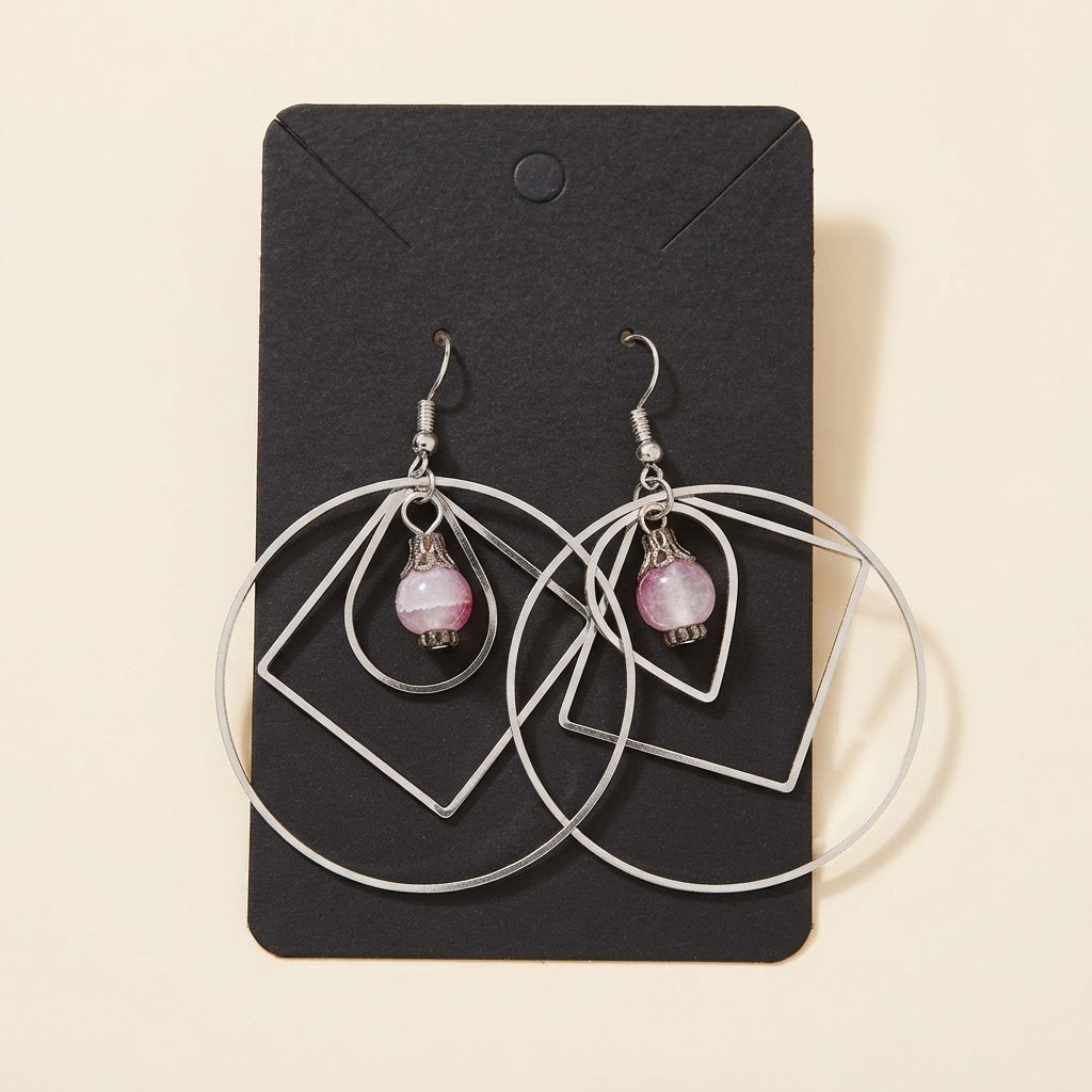 Boucles d’oreilles géométriques argentées avec perle rose sur fond studio