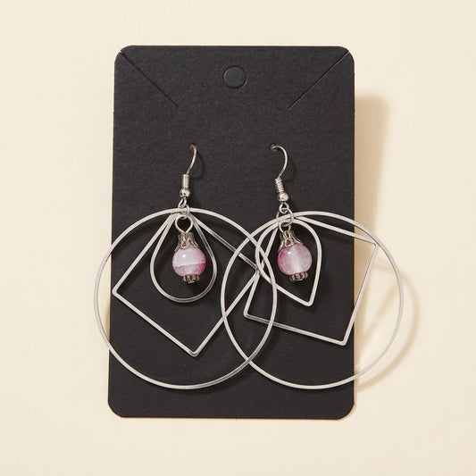 Boucles d’oreilles géométriques argentées avec perle rose sur fond studio