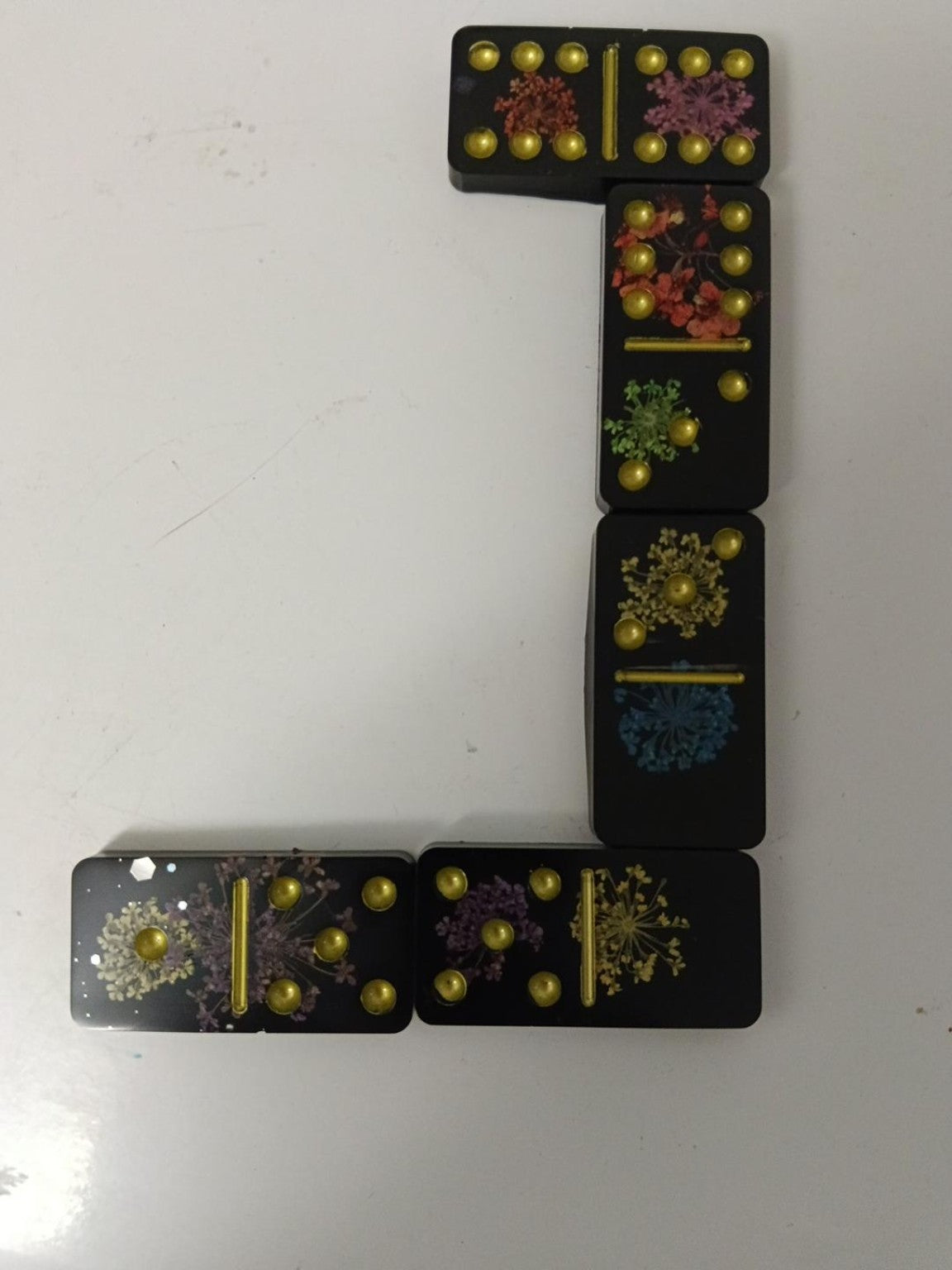 Détail du jeu de dominos en résine noire, fleurs colorées et points dorés