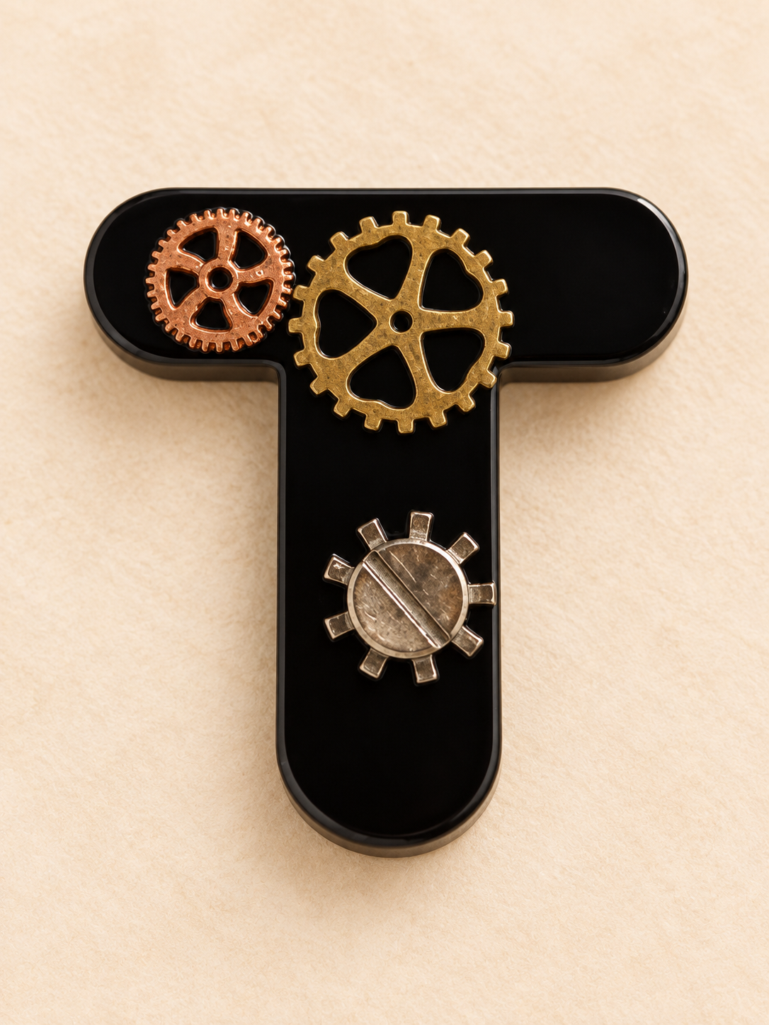 Détail d'une lettre T en résine noire décorée d'engrenages style steampunk