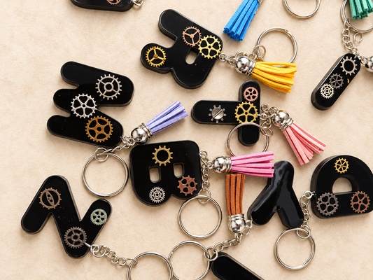 Porte-clés lettres en résine noire style steampunk avec engrenages et pompons colorés